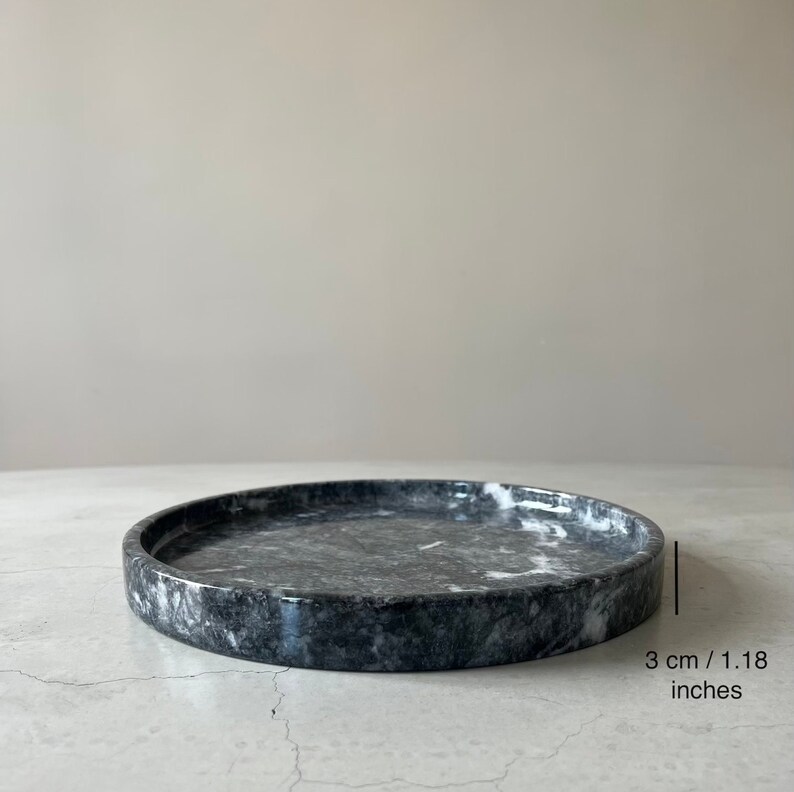 May include: A round, gray marble tray with white veining. The tray is 3 inches in diameter.