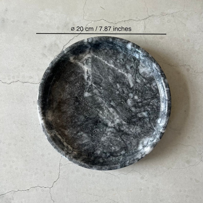 May include: A round, gray marble tray with a white marbled pattern. The tray measures 7.87 inches in diameter.