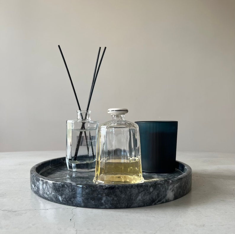 May include: A black marble tray with two glass bottles and a dark blue candle. The bottles are clear and contain liquid. The candle is in a ribbed glass container.