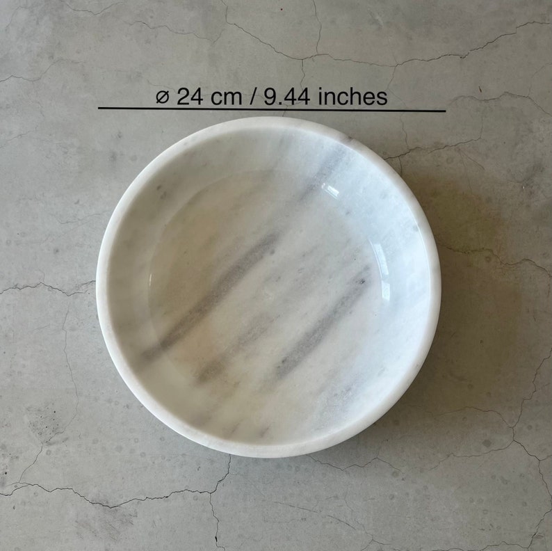 May include: A white marble bowl with gray veining. The bowl is 9.44 inches in diameter.