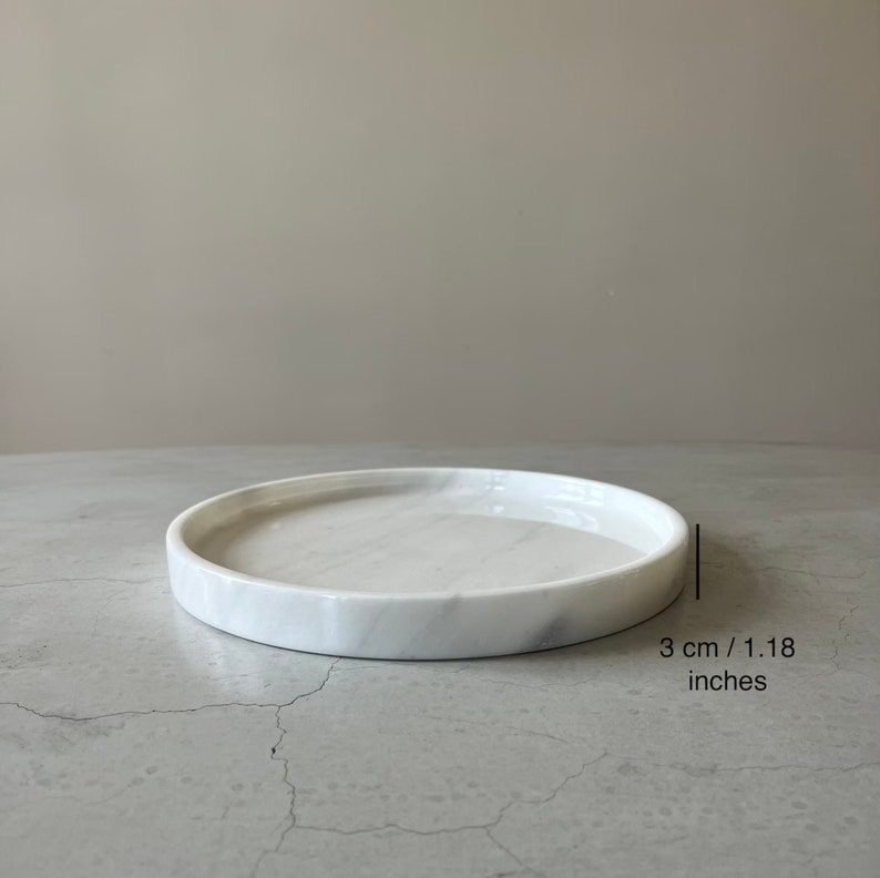 Pode incluir: Bandeja redonda de m&aacute;rmore branco com borda elevada. A bandeja tem um di&acirc;metro de 3 cm.