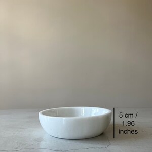 May include: A white ceramic bowl with a slightly rounded rim. The bowl is 5 cm / 1.96 inches in diameter.