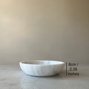 May include: White marble bowl with a smooth, rounded surface. The bowl is 6 cm / 2.36 inches in diameter.