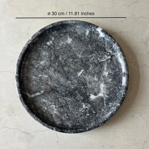 May include: A round, gray marble serving tray with white veining. The tray measures 11.81 inches in diameter.