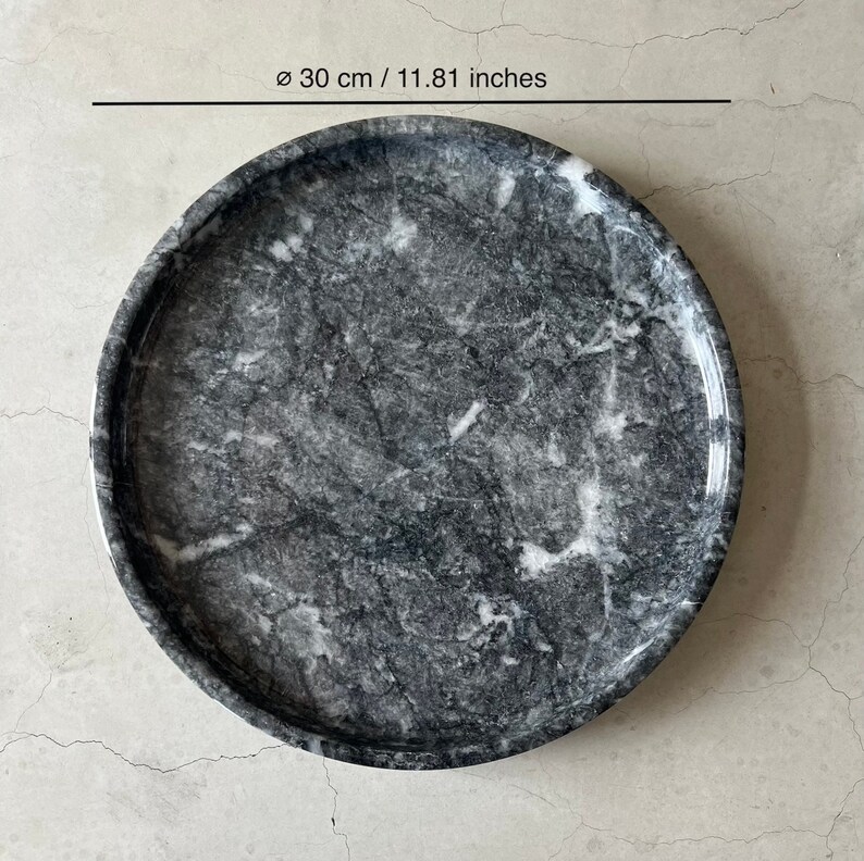 May include: A round, gray marble serving tray with white veining. The tray measures 11.81 inches in diameter.