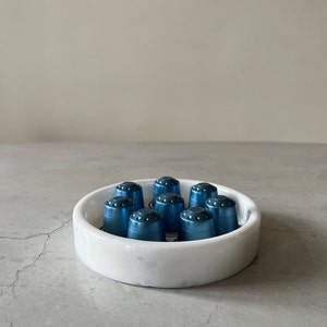 Pode incluir: Um prato de m&aacute;rmore branco com um design azul e branco cont&eacute;m dez c&aacute;psulas de caf&eacute; de metal azul.