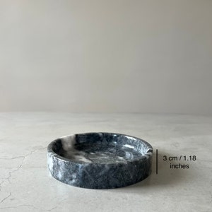 May include: A small, round, black and white marble dish with a diameter of 3 inches. The dish is made of natural stone and has a smooth, polished finish.