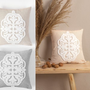 Peut inclure: Deux coussins décoratifs avec un motif floral blanc brodé. Le coussin de gauche est gris et le coussin de droite est beige.
