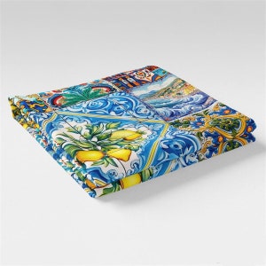 May include: A folded blue and white patterned fabric with yellow lemons and a scene of a coastal town. The fabric has a tile-like design.