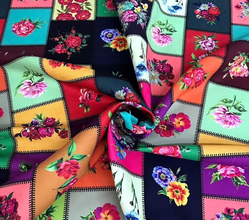 May include: A colorful floral fabric with a patchwork design. Each square features a different arrangement of roses, peonies, and other flowers in shades of pink, red, yellow, and purple. The fabric is folded, revealing a vibrant array of colors.