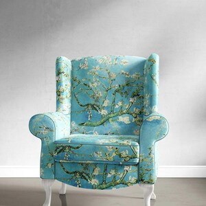 May include: A blue armchair with white legs and a floral print featuring a blooming almond tree. The fabric is a light blue with a white background and features a green tree with white blossoms.