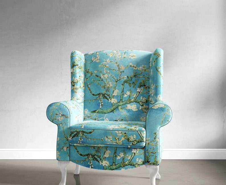 May include: A blue armchair with white legs and a floral print featuring a blooming almond tree. The fabric is a light blue with a white background and features a green tree with white blossoms.