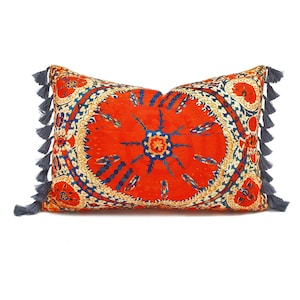 Peut inclure: Coussin de décoration orange et bleu à motifs avec des glands gris. Le coussin présente un motif circulaire avec des détails complexes.