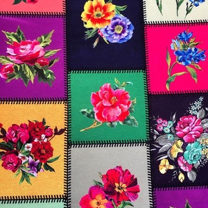 May include: A patchwork design featuring squares of various colors, each adorned with a vibrant floral arrangement. The flowers, in shades of red, pink, blue, and yellow, are set against backgrounds of purple, green, and other hues. Black stitching outlines each square.