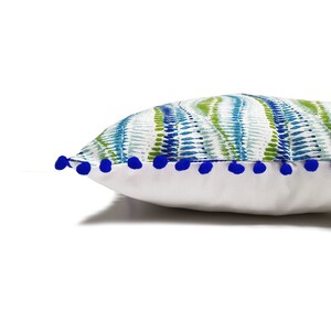 Peut inclure: Un oreiller blanc avec un motif abstrait bleu et vert et une bordure de pompons bleus.