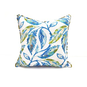 Peut inclure: Un coussin blanc avec un motif de feuilles bleues et vertes. Le coussin a une bordure dor&eacute;e.