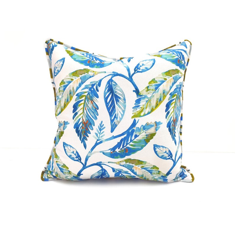 Peut inclure: Un coussin blanc avec un motif de feuilles bleues et vertes. Le coussin a une bordure dor&eacute;e.