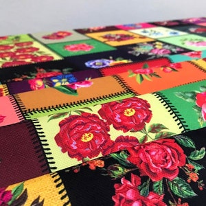 May include: A colorful patchwork textile featuring a variety of floral patterns. The design incorporates squares and rectangles with images of red roses, other flowers, and geometric shapes. The edges of each patch are stitched with black thread.