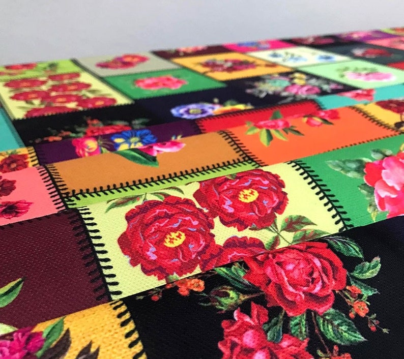 May include: A colorful patchwork textile featuring a variety of floral patterns. The design incorporates squares and rectangles with images of red roses, other flowers, and geometric shapes. The edges of each patch are stitched with black thread.