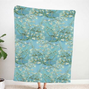 May include: A blue and white throw blanket with a repeating pattern of blooming almond trees. The pattern is inspired by a famous painting.