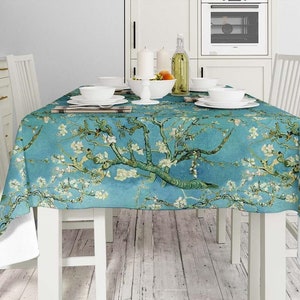 May include: A blue tablecloth with a floral print of white blossoms and green branches. The tablecloth is laid on a white table with four white chairs.