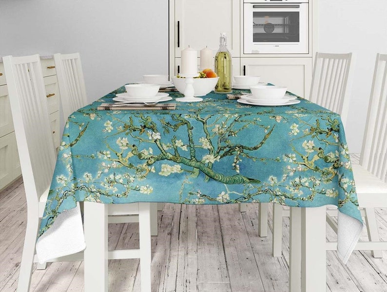 May include: A blue tablecloth with a floral print of white blossoms and green branches. The tablecloth is laid on a white table with four white chairs.