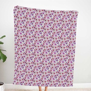 May include: A white throw blanket with a repeating pattern of purple and pink passion fruit. The fruit is surrounded by a black outline and a white background.