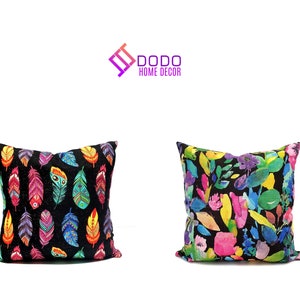 Peut inclure: Deux coussins décoratifs avec un fond noir et des motifs colorés. Un coussin présente un motif répétitif de plumes colorées, tandis que l'autre coussin présente un motif répétitif de fleurs et de feuilles colorées.  DODO HOME DECOR est imprimé en texte violet sur fond blanc.