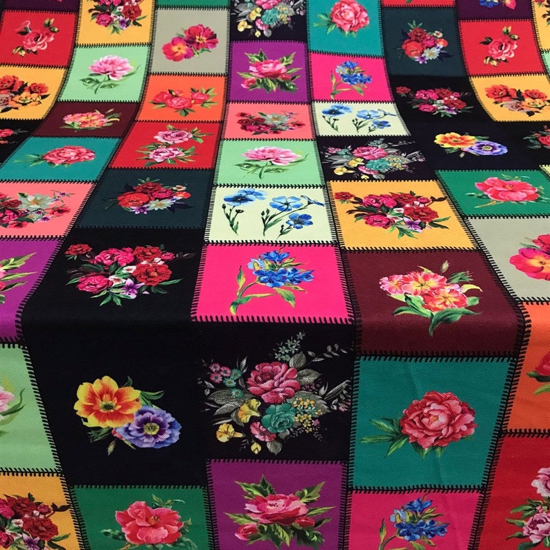 May include: A colorful patchwork textile featuring a repeating pattern of floral bouquets. Each square showcases a different arrangement of flowers in vibrant hues like red, pink, yellow, and blue, set against a black background. The squares are outlined with black stitching.