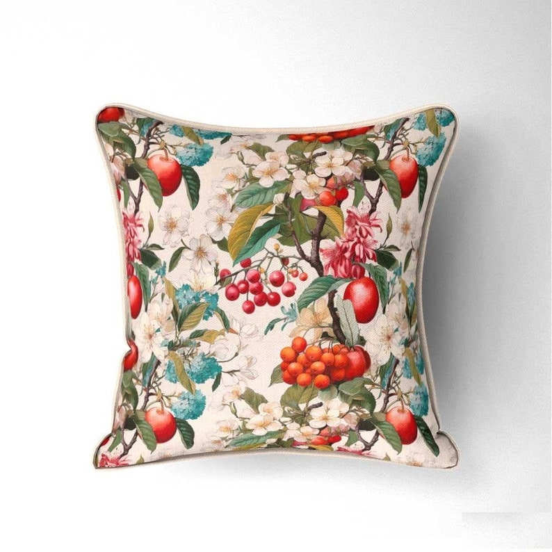 May include: A square cushion with a cream background and a floral print featuring red apples, red berries, and white flowers.