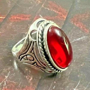 May include: A silver ring featuring an oval red gemstone set in an intricate silver design.