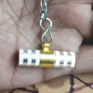 May include: A silver and gold cylindrical charm with a chain attached. The charm has a ridged design and is about 2 inches long.