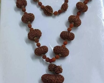 May include: A brown mala necklace with a silver pendant featuring a swastika symbol. The necklace is made of round beads with a textured surface.