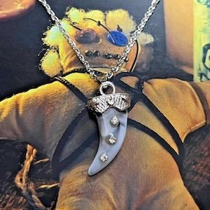 May include: A silver chain necklace with a white and silver tooth pendant with three clear rhinestones.