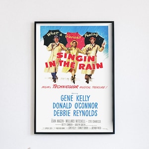 Pode incluir: Um cartaz de filme vintage emoldurado para "Singin' in the Rain". O cartaz apresenta três pessoas em capas de chuva e chapéus sob guarda-chuvas. O título está em letras vermelhas grandes. O cartaz também lista as estrelas e os créditos de produção.