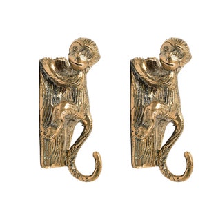 May include: Two gold monkey hooks, each with a monkey climbing a tree trunk and holding a hook in its hand. The hooks are made of metal and have a shiny finish.