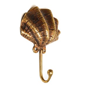 May include: A gold-toned metal hook shaped like a seashell. The hook is designed to hang items on a wall.