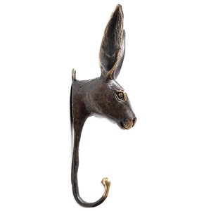 May include: A bronze rabbit head wall hook with a gold-toned hook. The rabbit's head is facing to the right and the hook is curved.