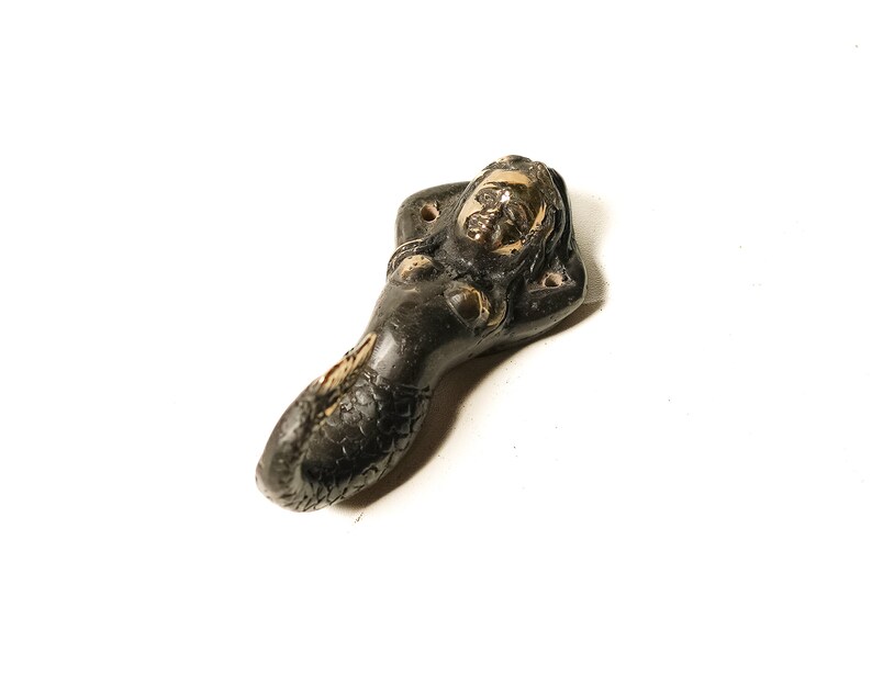 May include: A black and gold mermaid figurine with a long tail and a relaxed pose. The figurine is made of metal and has a detailed design.