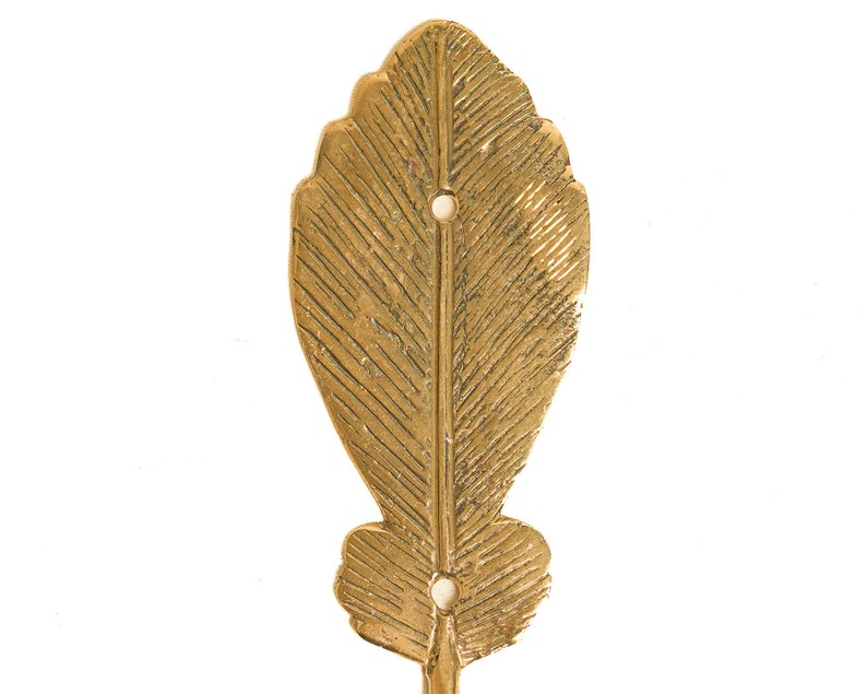 May include: Gold metal leaf-shaped wall hook with a textured surface. The hook has two holes for hanging.