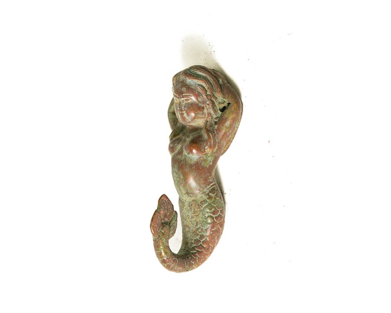 May include: A bronze mermaid figurine with a green patina. The mermaid is depicted with long flowing hair and a tail with scales.