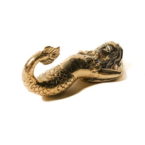May include: A gold-coloured mermaid figurine with a detailed tail and a reclining pose.