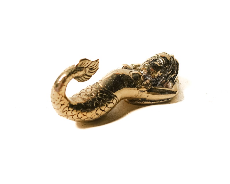 May include: A gold-coloured mermaid figurine with a detailed tail and a reclining pose.