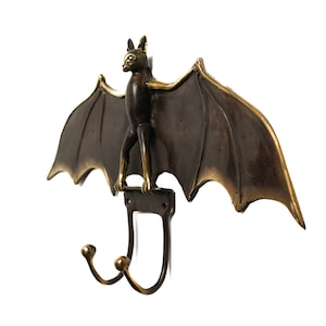 May include: A brass bat wall hook with two hooks. The bat is in a flying position with its wings spread out. The bat is dark brown with gold accents.