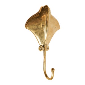 May include: A gold-coloured metal wall hook shaped like a stingray. The hook has a curved tail that forms a hook.