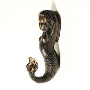 May include: A black and gold mermaid figurine with a detailed tail and a gold crown. The mermaid is standing with her arms raised above her head.