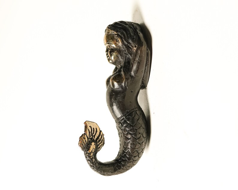 May include: A black and gold mermaid figurine with a detailed tail and a gold crown. The mermaid is standing with her arms raised above her head.