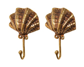 May include: Two gold-toned metal hooks shaped like seashells. The hooks are designed to be mounted on a wall.