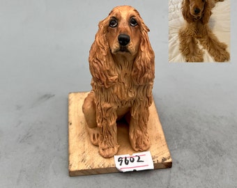 May include: A ceramic figurine of a brown and white cocker spaniel dog sitting on a wooden base. The figurine is detailed with realistic fur and features. The base has a price tag that reads "9602".