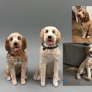 May include: Two custom-made dog sculptures, one brown and white and one light brown, are sitting on a grey surface. The sculptures are realistic and detailed, capturing the dogs' unique features.